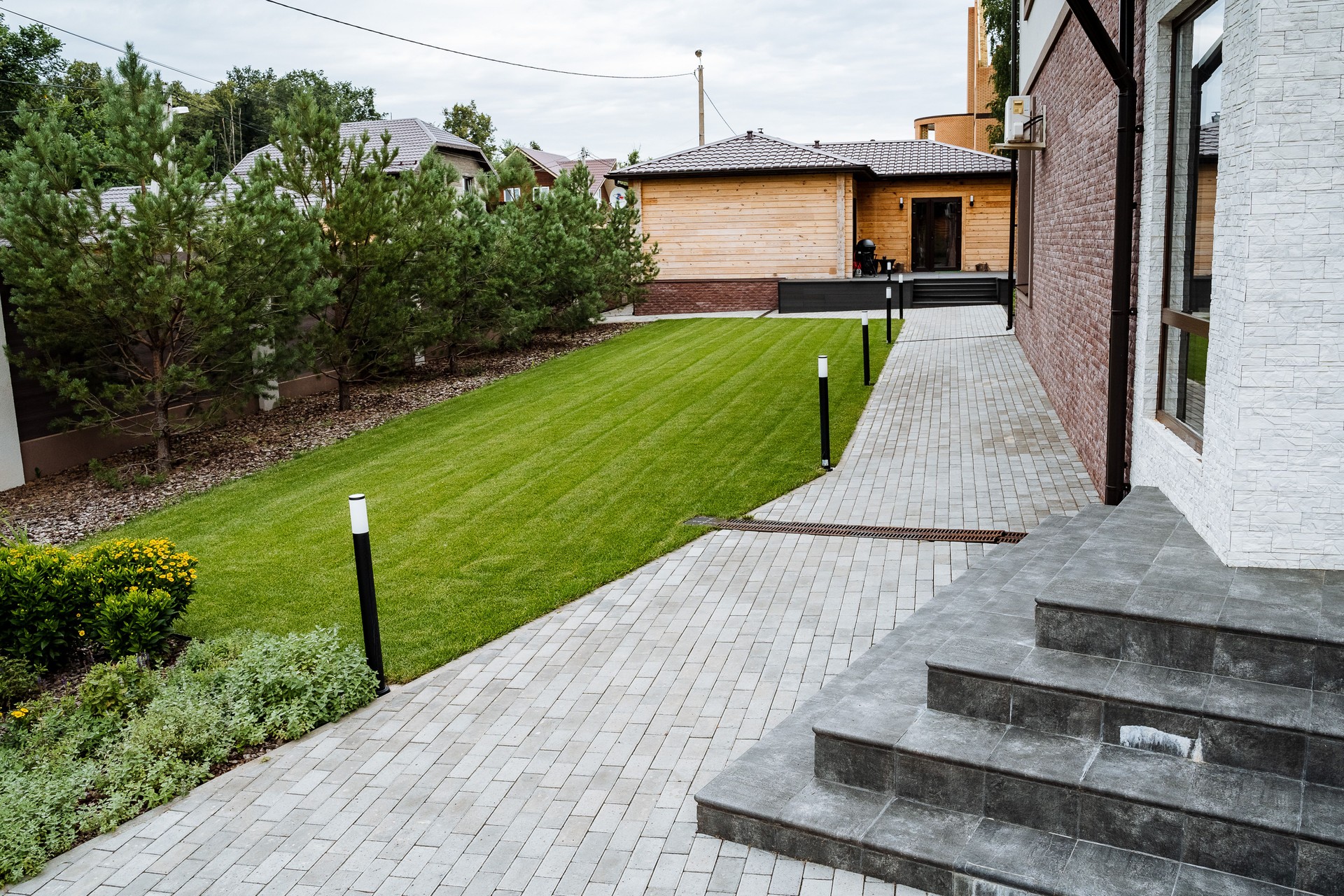 This stunningly beautifully landscaped backyard features a charming paved pathway accompanied by a vibrant green lawn filled with life